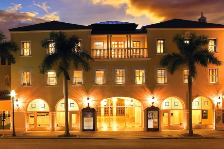 Illuminated opera house facade at dusk with palm trees and a marquee sign.