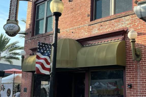 Brick building facade with a green awning, American flag, and vintage-style streetlamp.