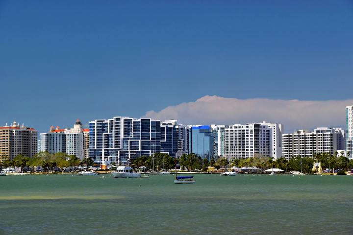 Skyline with modern high-rise buildings and boats on a sunny waterfront.
